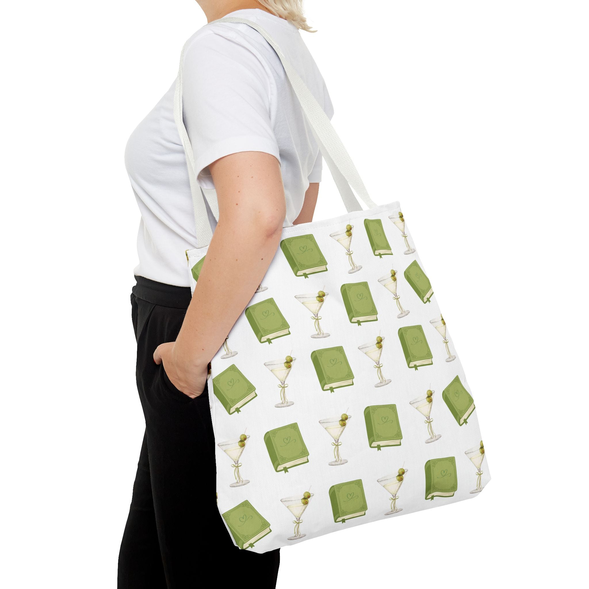 Person holding a tote bag with green book and martini glass pattern on a white background