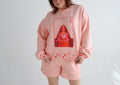 A woman modeling a light pink lounge set consisting of a sweatshirt and matching shorts, featuring a red playing card graphic on the sweatshirt and small red hearts along the hem.