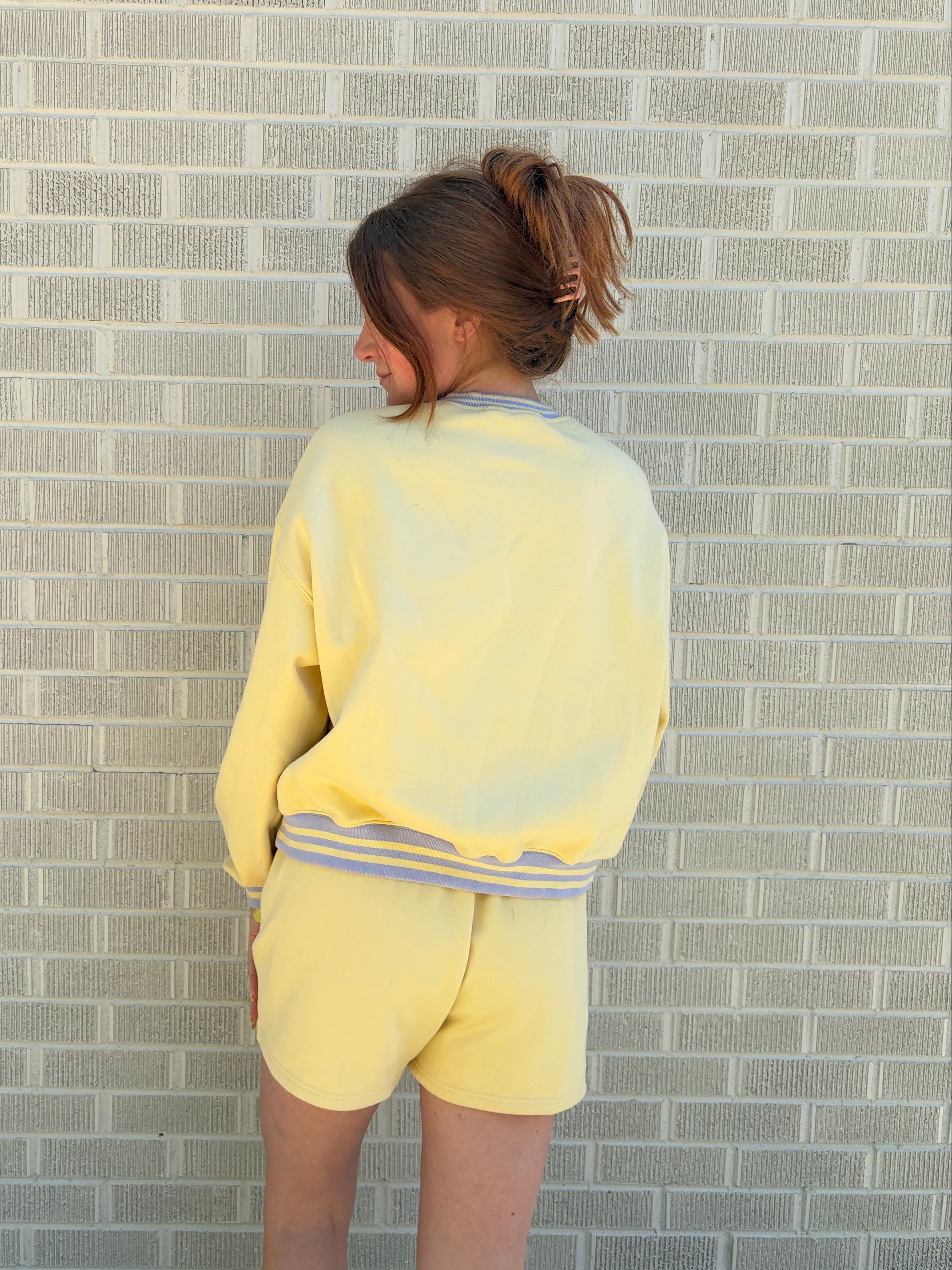 Person wearing a yellow outfit standing against a gray brick wall