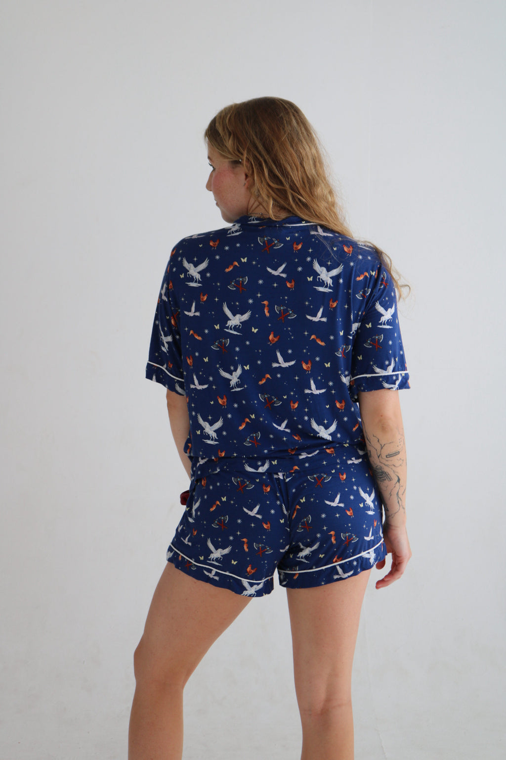 A woman wearing a navy blue pajama set with a white and orange space-themed print of planets, stars, and rockets, shown from a side profile against a plain light gray background.