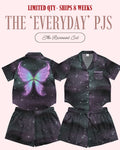 A product listing graphic for a children's pajama set labeled 'The Everyday PJS' and 'The Revenant Set,' showing two views of a matching short-sleeve top and shorts set on a pale pink background. The pajama set has a dark galaxy print with a large purple and blue butterfly graphic on the left shirt view, and a small white embroidered 'Revenant' on the right shirt chest.
