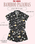 A two-piece pajama set displayed on a pale pink background with promotional text. The pajama set includes a short-sleeve button-up top and matching shorts in black with a whimsical celestial print of moons, stars, clouds, and small illustrated characters.