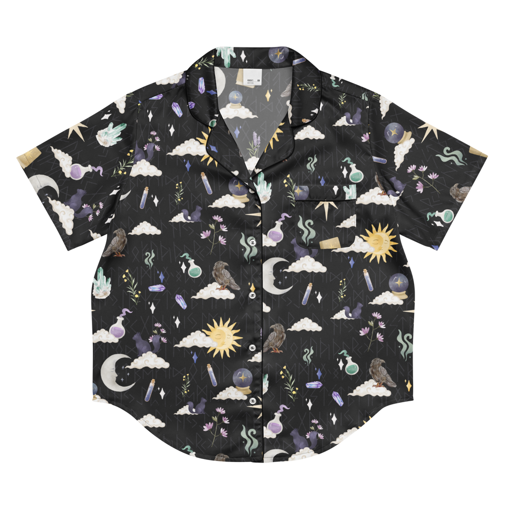 A short-sleeve button-up shirt with a dark charcoal/black background and an all-over mystical celestial print featuring clouds, moons, suns, birds, crystals, and herbs.
