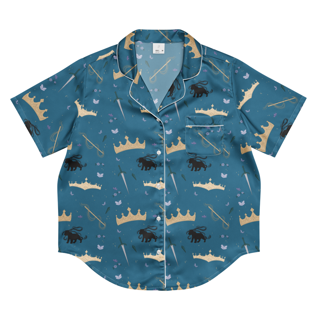 A short-sleeve button-up pajama shirt in teal blue with an all-over whimsical print of gold crowns, black lions, white birds, and white staffs, finished with white piping.